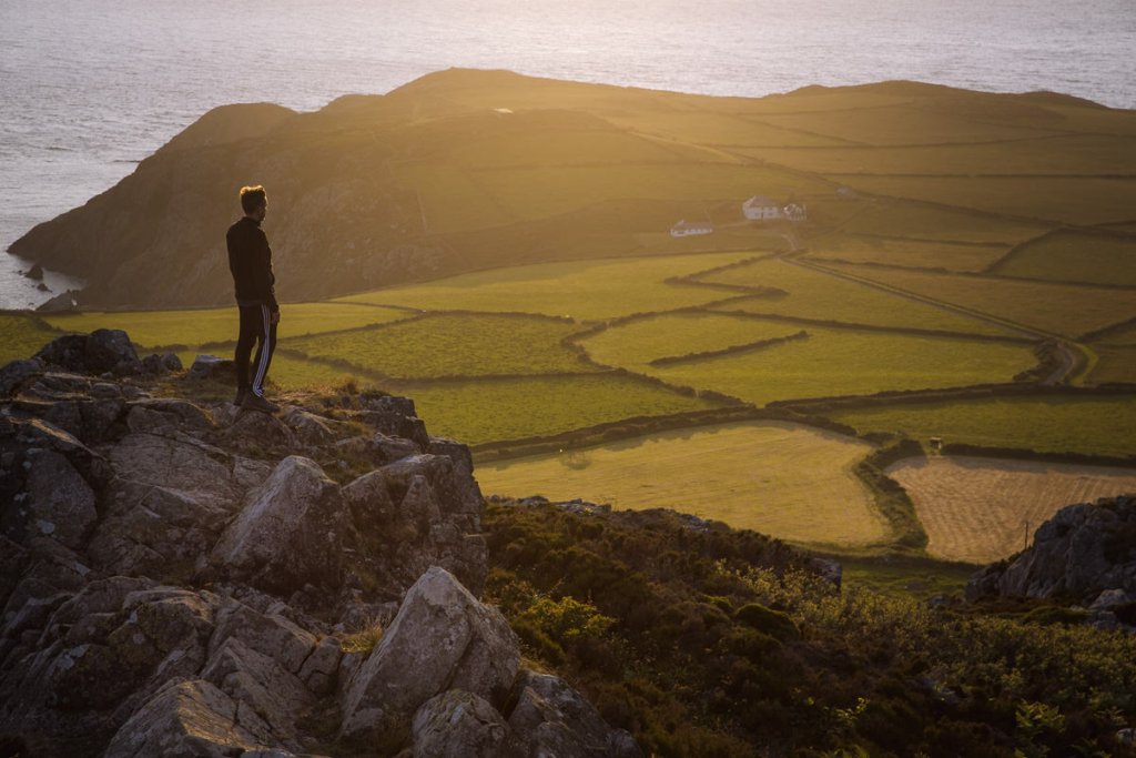 el hombre se encuentra en una roca con vistas a un mosaico de campos junto al mar