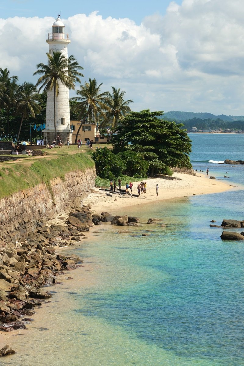 Un grupo de personas que juegan en la playa de arena al lado del faro de Galle, Sri Lanka.