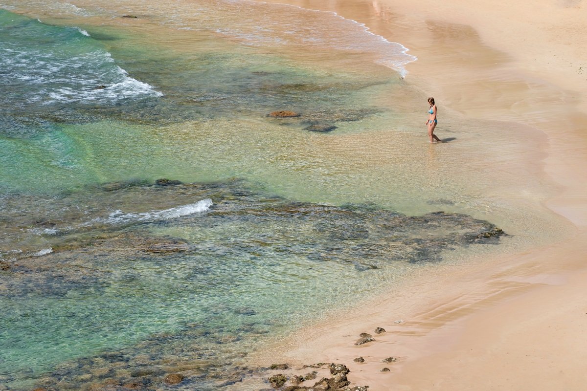 Un nadador con un traje de bañamiento turquesa que camina hacia el agua clara y poco profunda en Mirissa Beach, Sri Lanka.