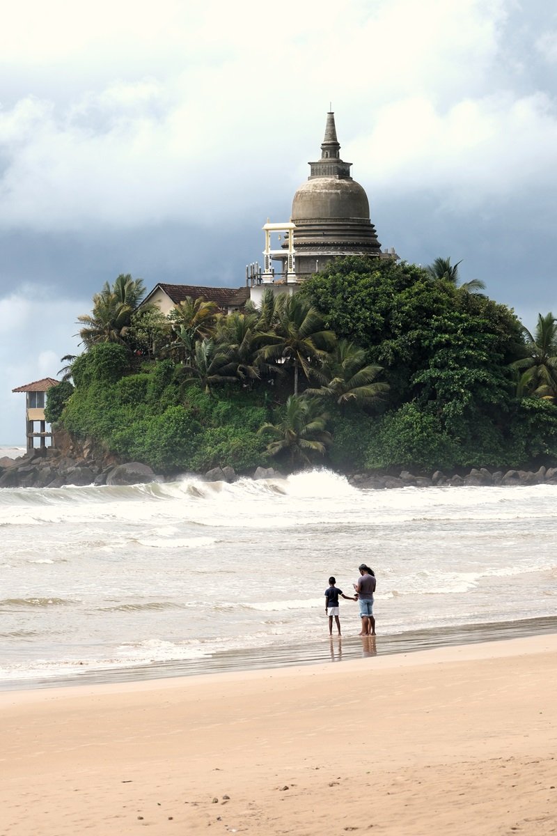 Una familia de pie en el agua frente a un templo remoto en Matara Beach en Sri Lanka.