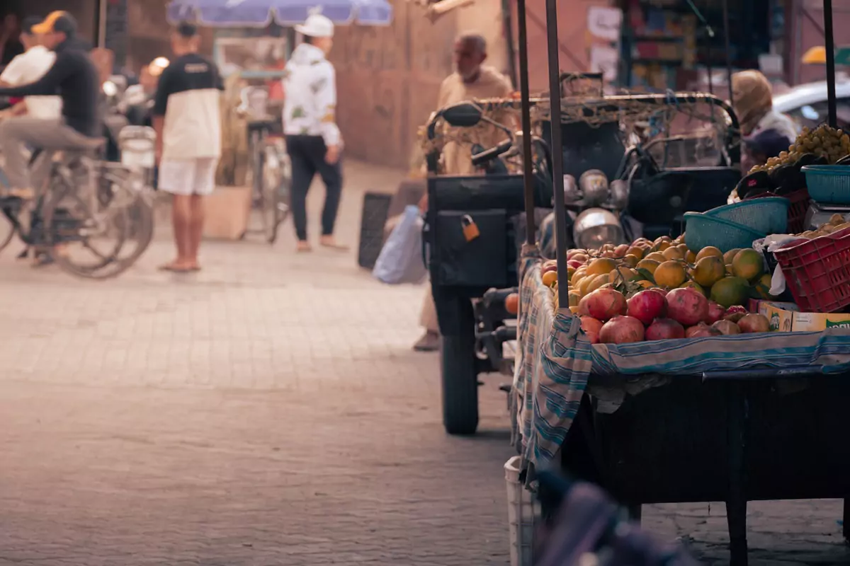 Un puesto de frutas con varias frutas en una tela azul y blanca en un mercado ocupado en Taroudant, Marruecos.