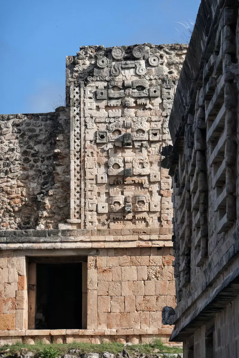 Intrincados grabados en piedra en la fachada de un edificio en Uxmal, que representan rostros con los dientes al descubierto.